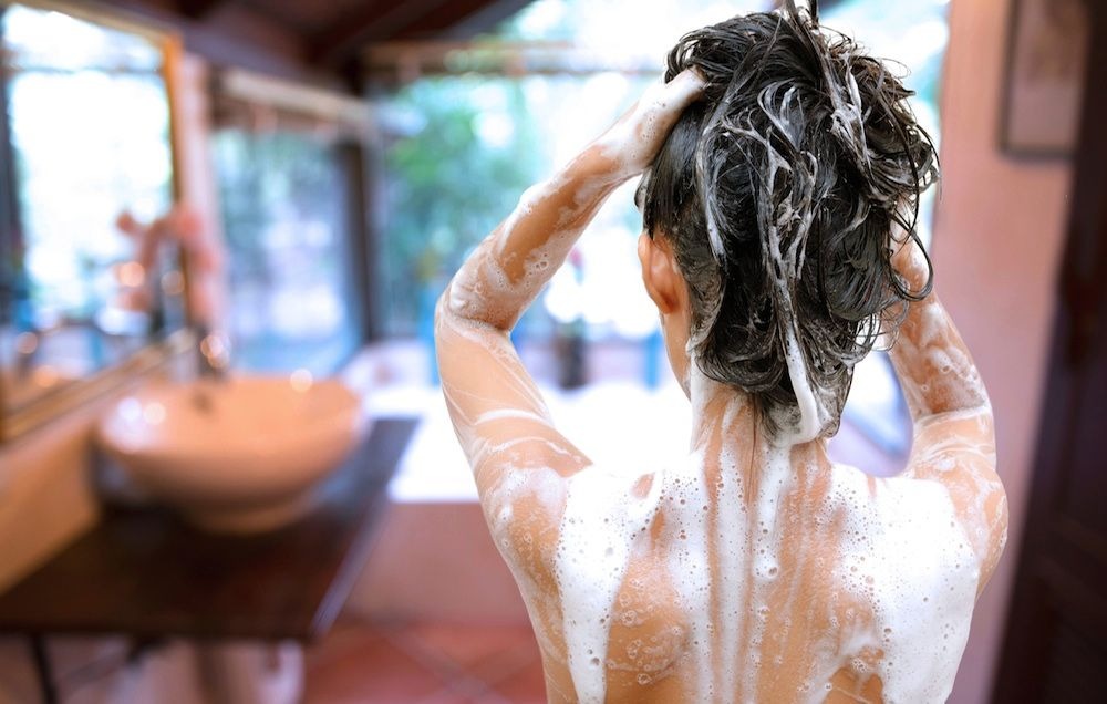 Person washing hair and body with shampoo suds.
