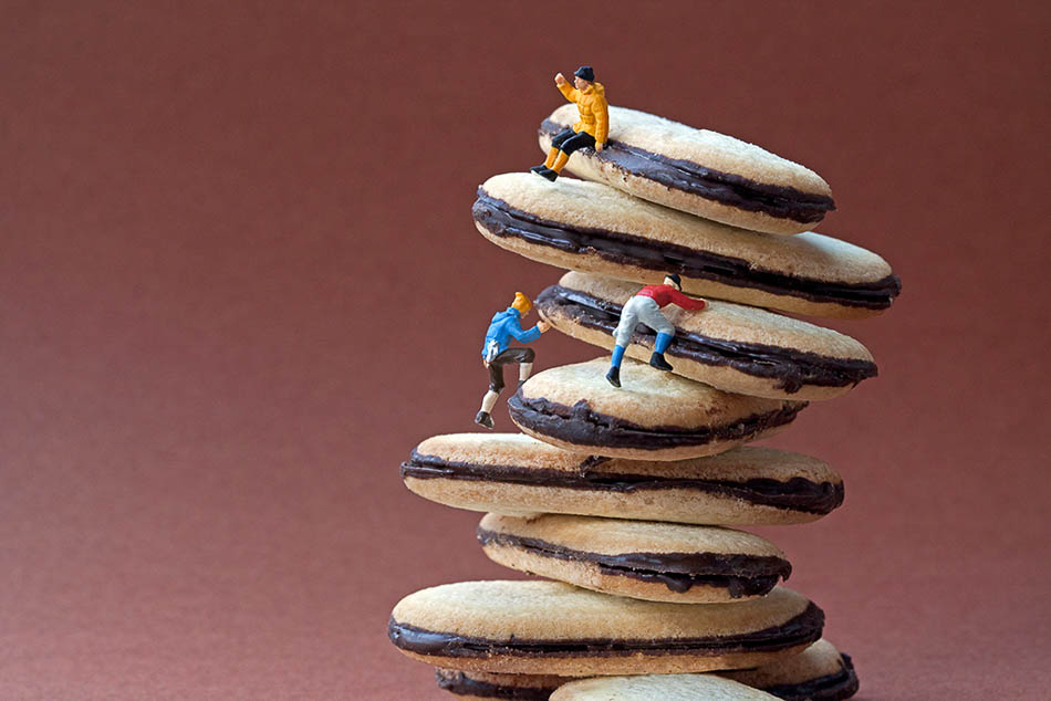Miniature figures climbing a stack of cream biscuits.