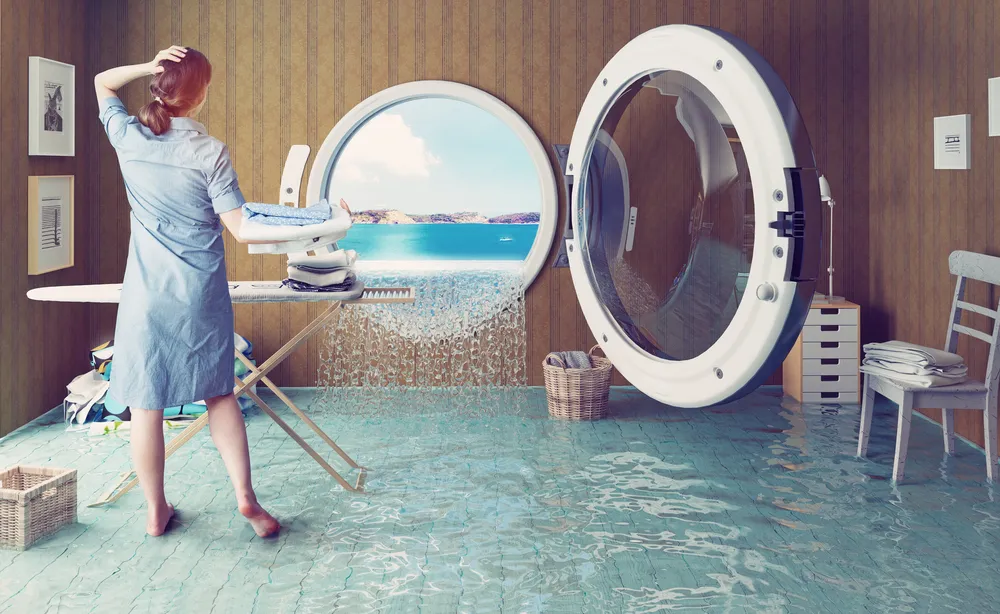 Surreal depiction of a laundry room with a woman standing in water, highlighting a washing machine and a window view of the ocean, symbolizing the link between household laundry and ocean pollution.