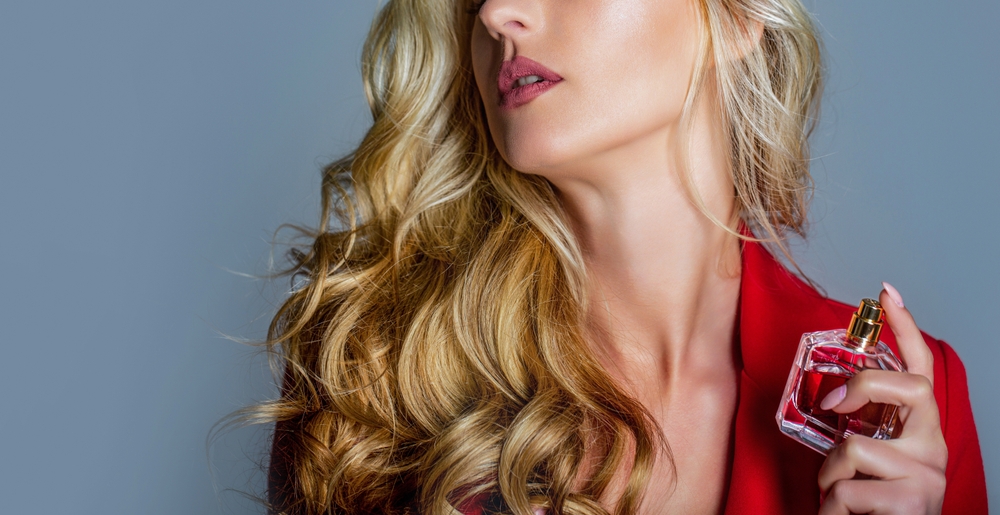 Woman holding perfume bottle, wearing red jacket.