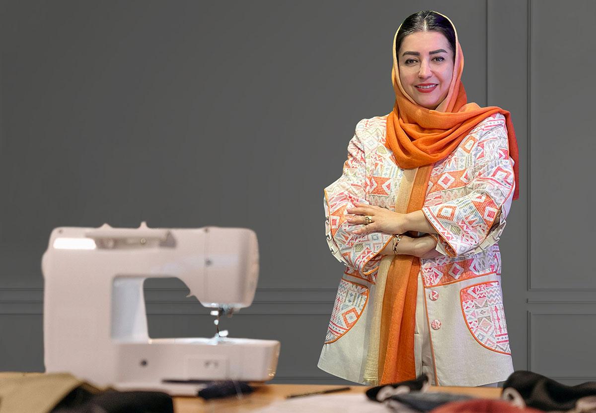 Woman in colourful robe, standing by sewing machine.