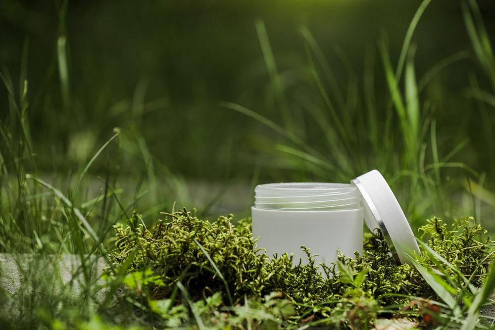 Open cream jar on grass and moss outdoors.