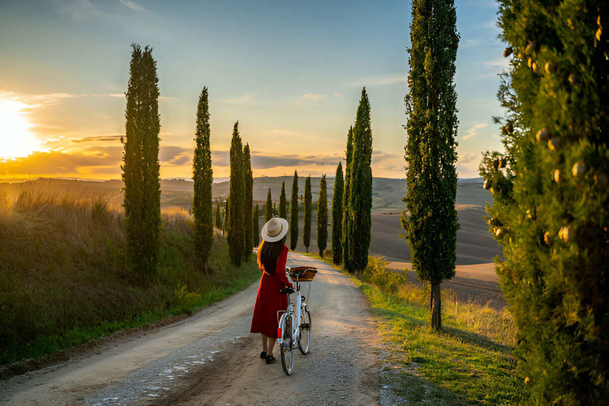 Woman with bicycle on country road at sunset