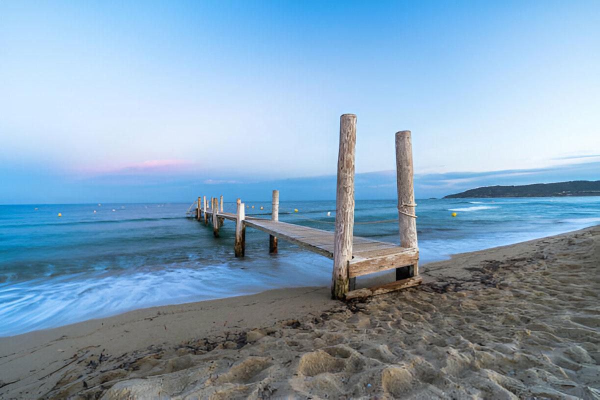 Wooden pier on sandy beach at sunset