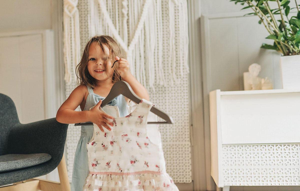 Young girl smiling, holding floral dress on hanger.