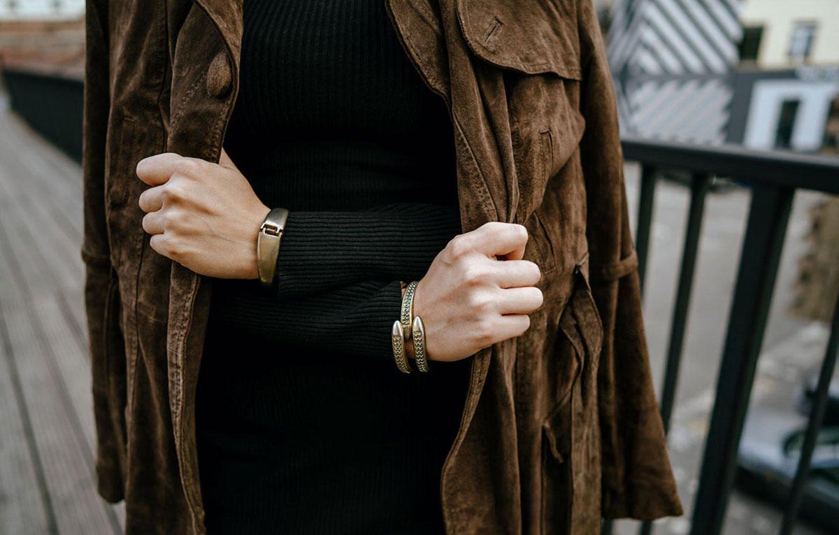 Person wearing brown coat and bracelets outdoors.