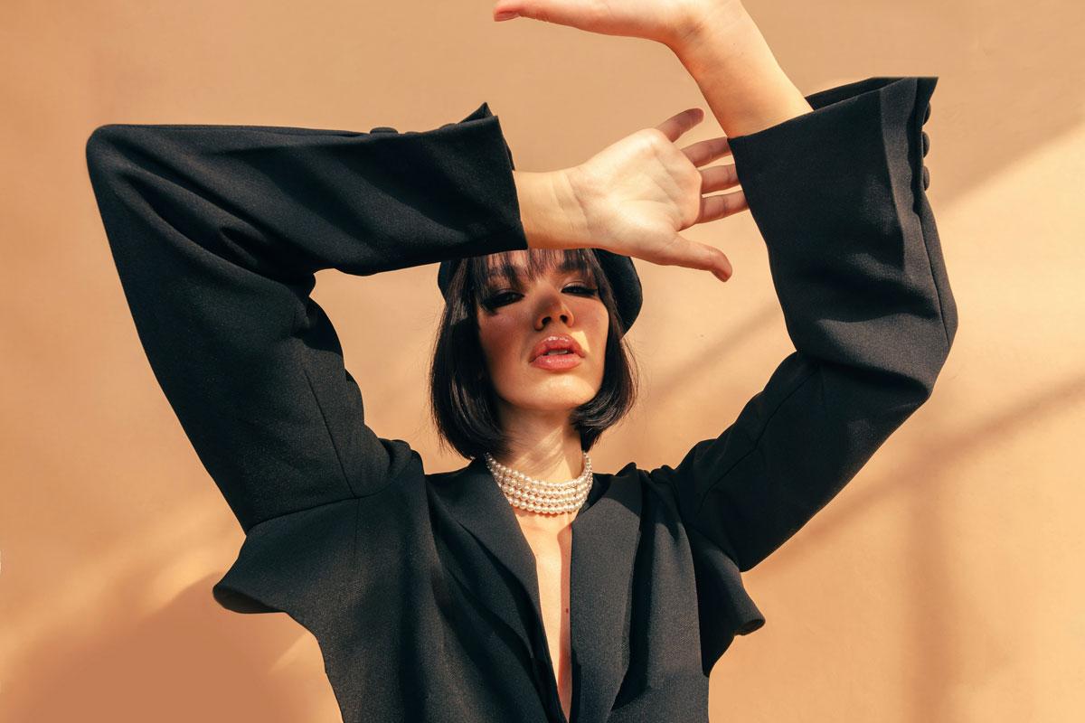 Woman posing in stylish black outfit, pearl necklace.