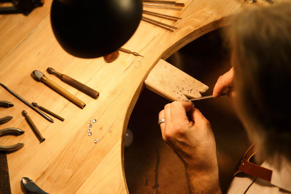 Jeweller crafting with tools on wooden bench.