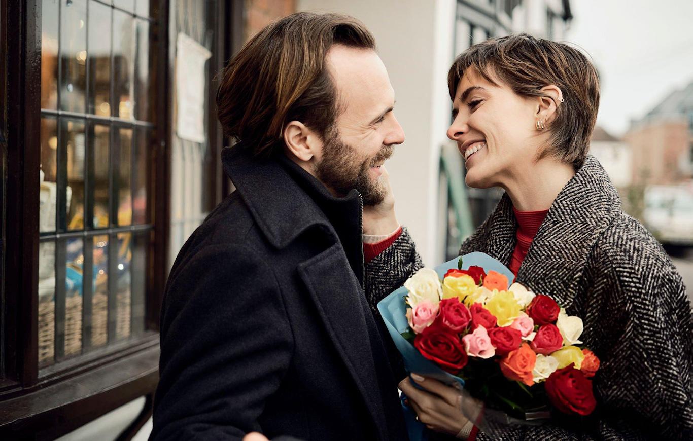 Smiling couple holding colourful flower bouquet.