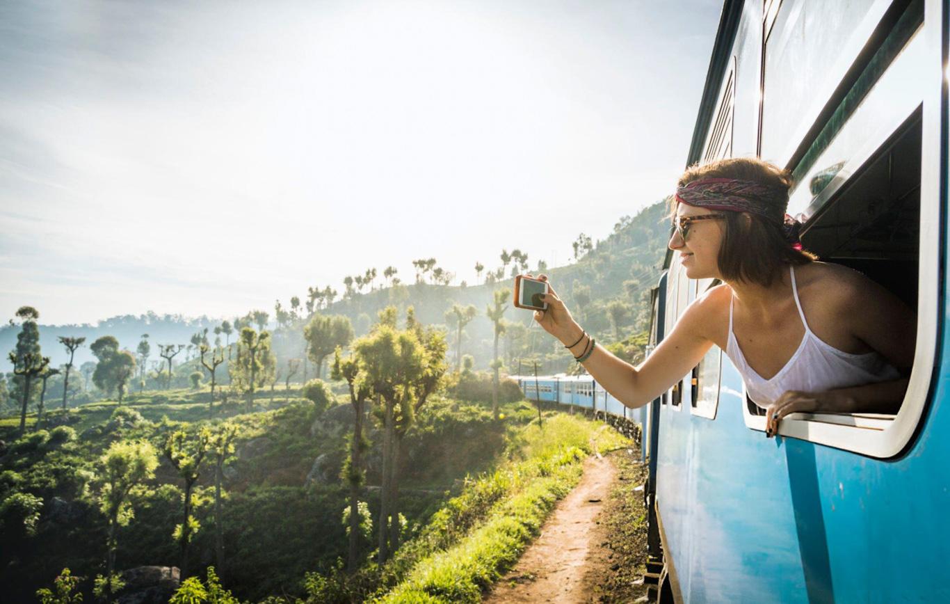 Woman on train taking photo of scenic landscape.
