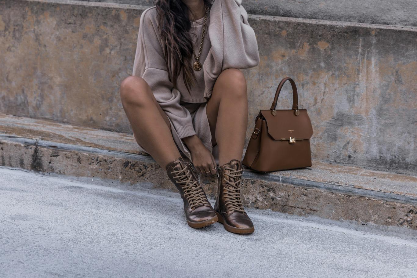 Woman in boots and bag sitting outdoors.