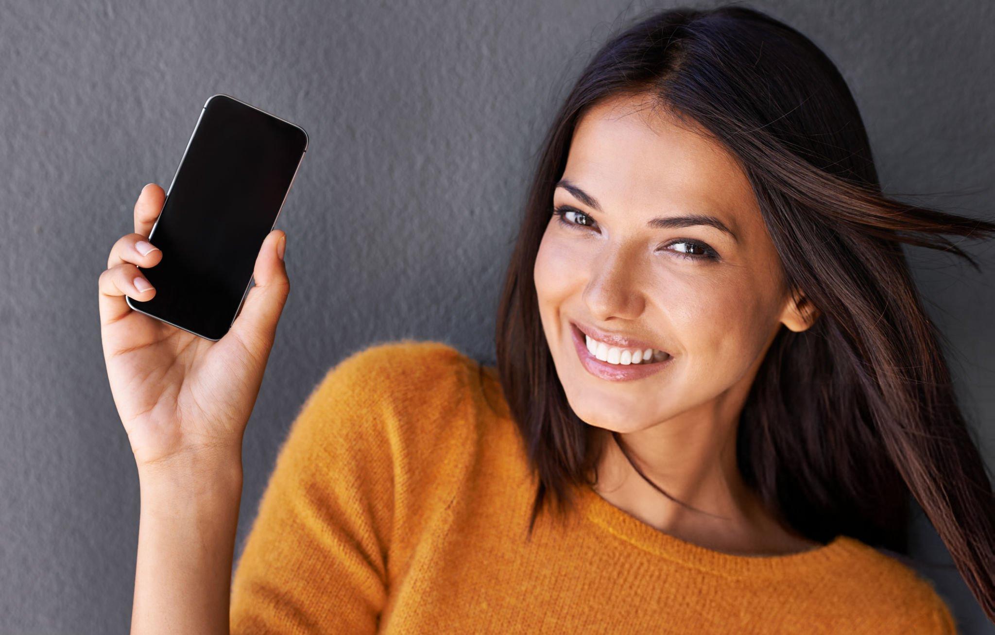 Smiling woman holding smartphone, grey background