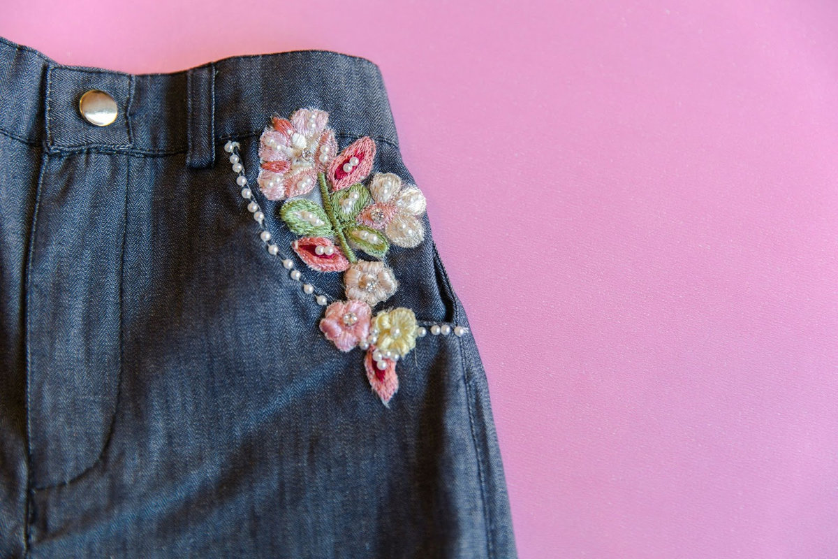 Denim jacket with delicate floral embroidery and pearl details on pink background, showcasing romantic flower fashion trends