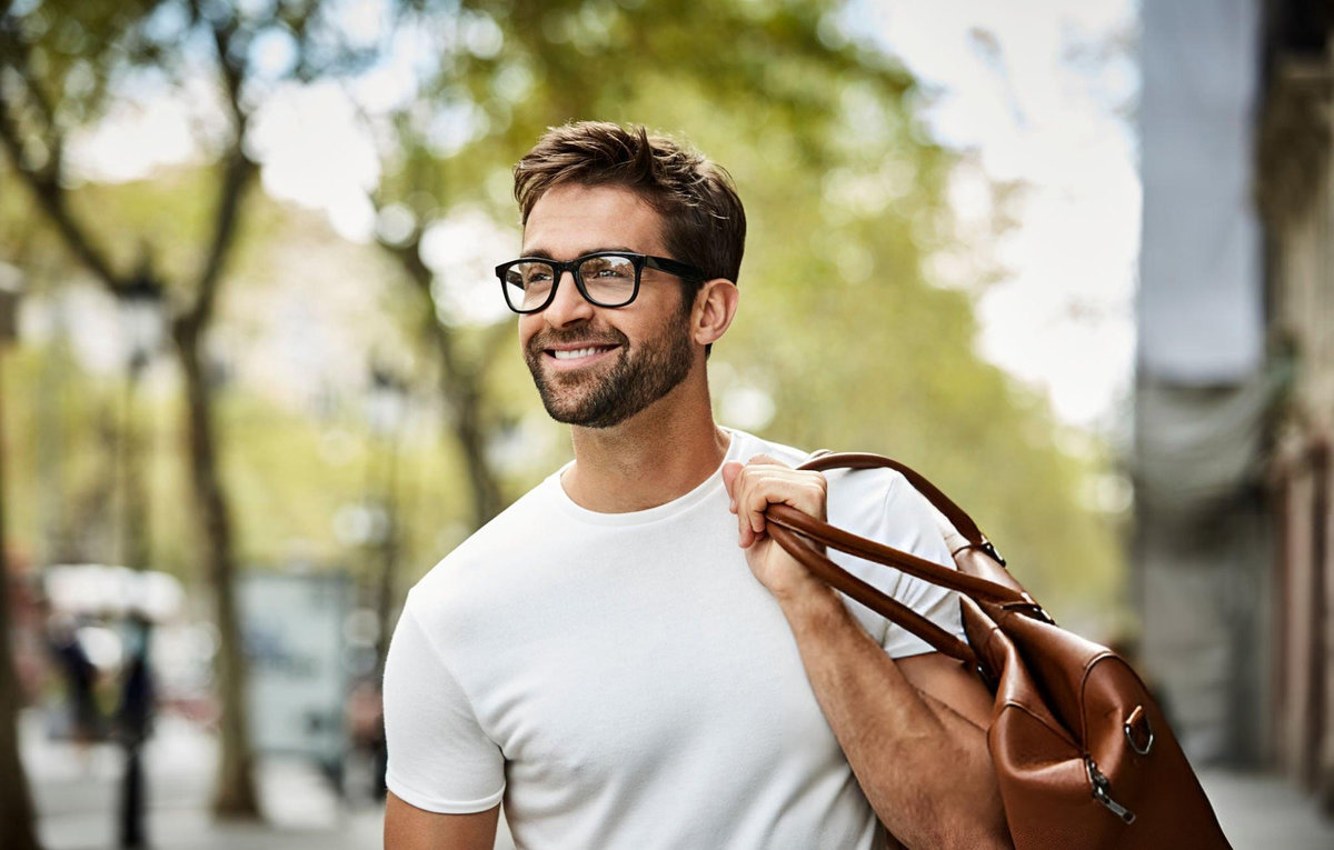 Smiling man with glasses carrying brown leather shoulder bag in urban setting, representing stylish minimalist personality type