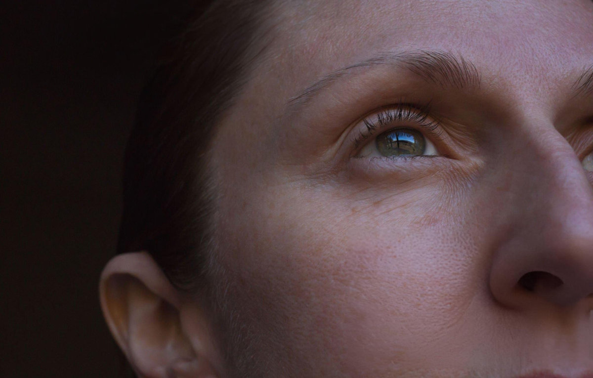 Close-up portrait showing natural skin texture and eye area, photographed in warm, natural lighting.