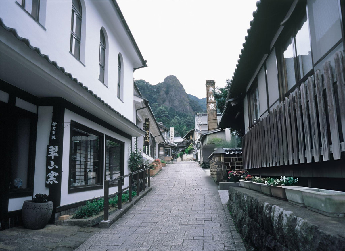 Cobblestone street in Okawachiyama pottery village showing traditional Japanese workshops with brick kiln chimney, demonstrating the Village of Secret Kilns where kintsugi potters abandoned wholesale for direct tourist sales