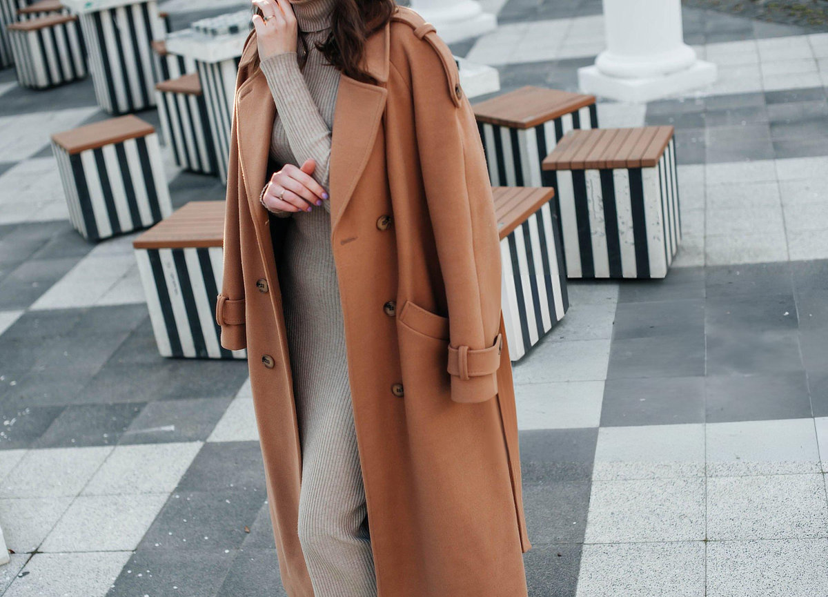 Woman wearing classic camel wool coat styled with ribbed beige knitwear demonstrating timeless winter luxury outerwear and elegant layering