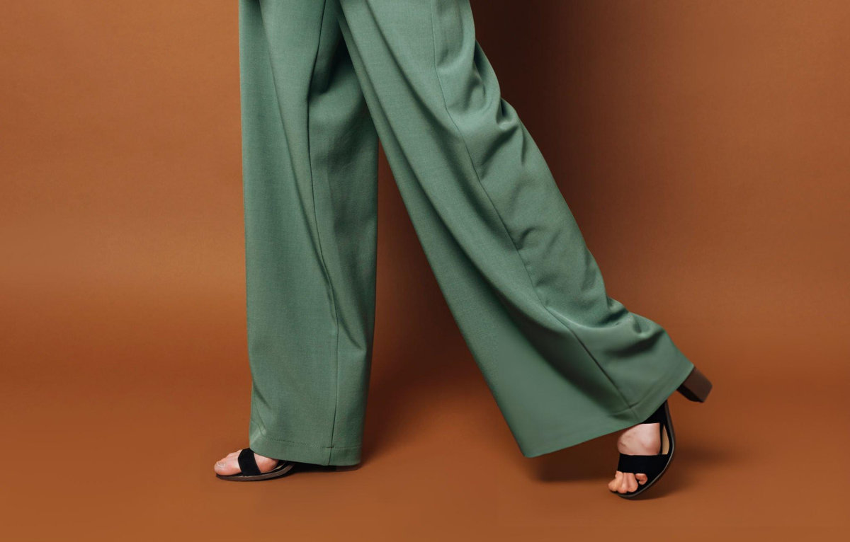 Wide-leg sage green trousers with relaxed fit on model wearing black sandals, representing inclusive sizing and sustainable fashion design principles