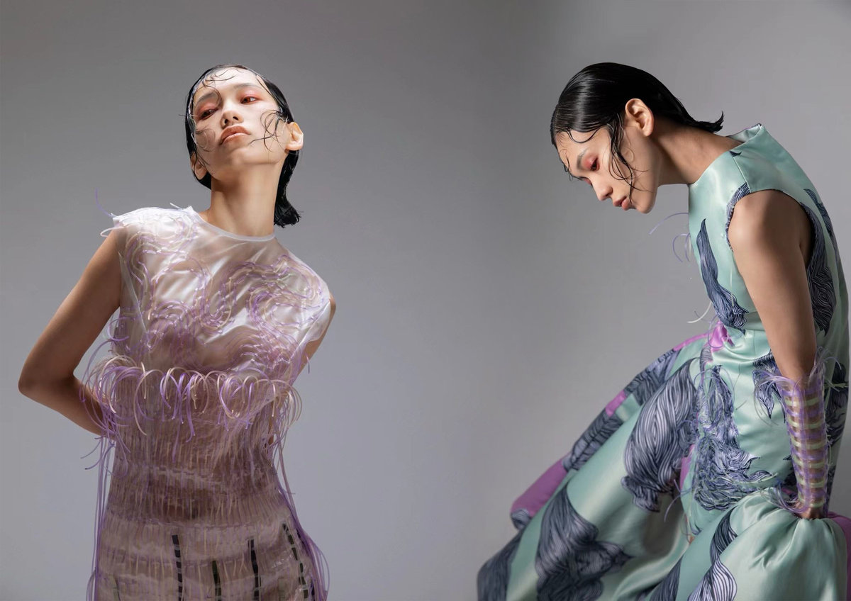 Two models showcasing Alimujiang Adili's contemporary designs - one in lavender translucent sleeveless dress with organic textures, another in mint green printed garment with flowing silhouette