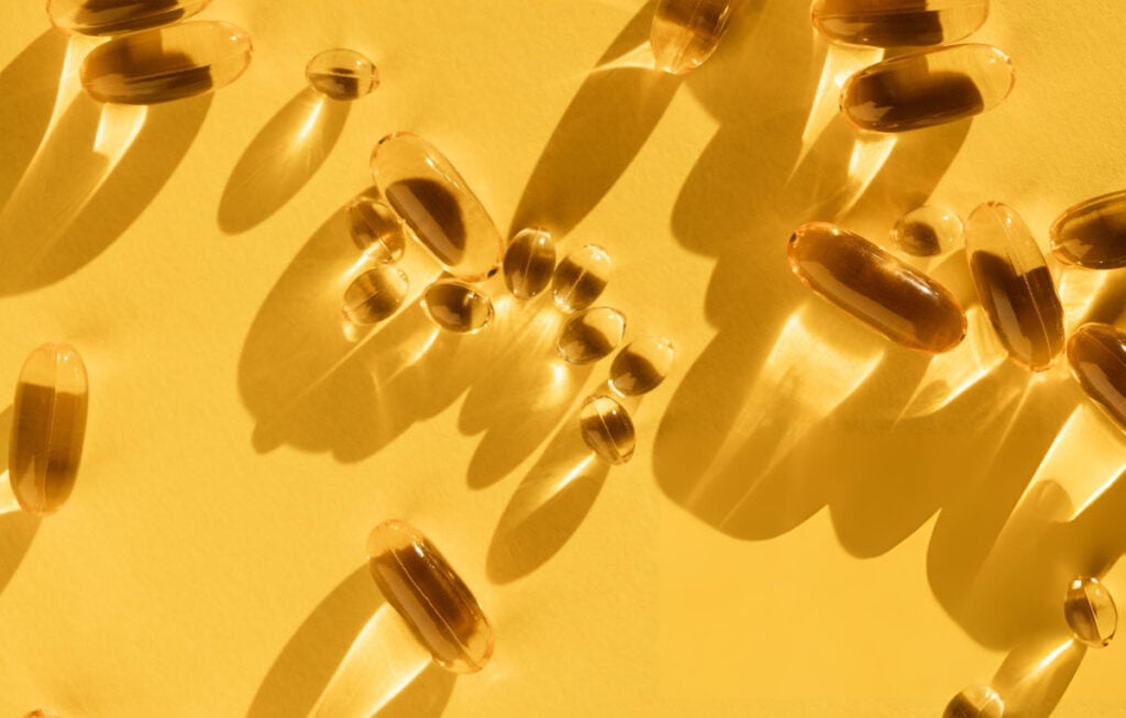Vitamin D softgel capsules on a yellow background, illustrating high-dose vitamin D supplements examined in Zittermann vitamin D research.