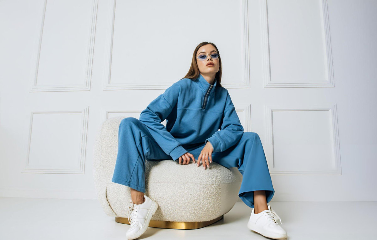 Woman in blue co-ord set seated on boucle ottoman — fashion e-commerce editorial