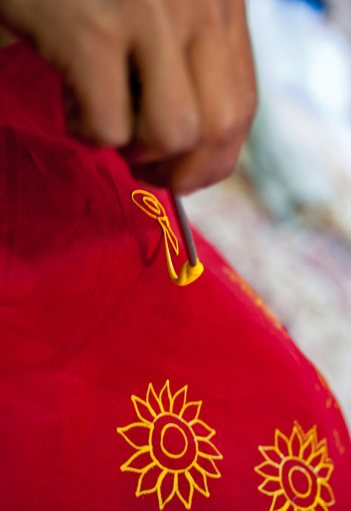An artisan applies rogan paint to red fabric using a metal stylus