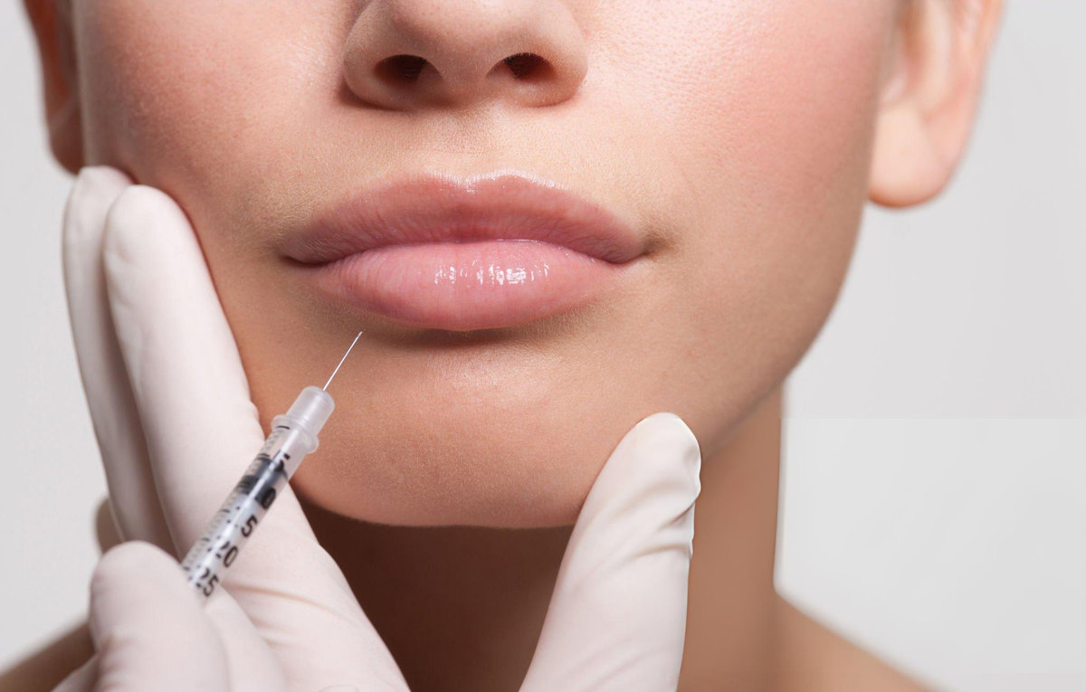 Gloved practitioner administering a facial injection near the lip area during a professional aesthetic procedure