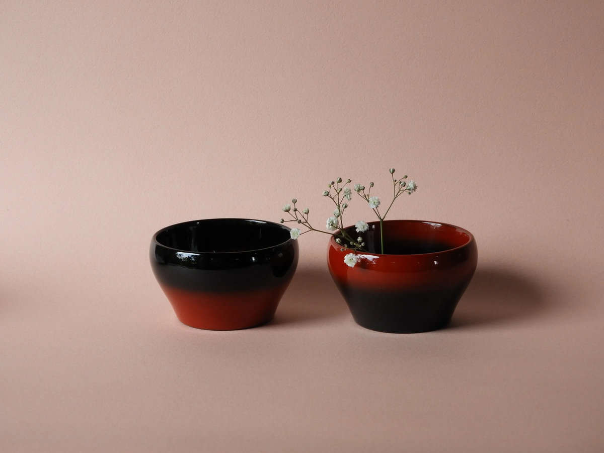 Two urushi lacquerware bowls in black and deep red, one holding small white gypsophila flowers — The Fashion Globe