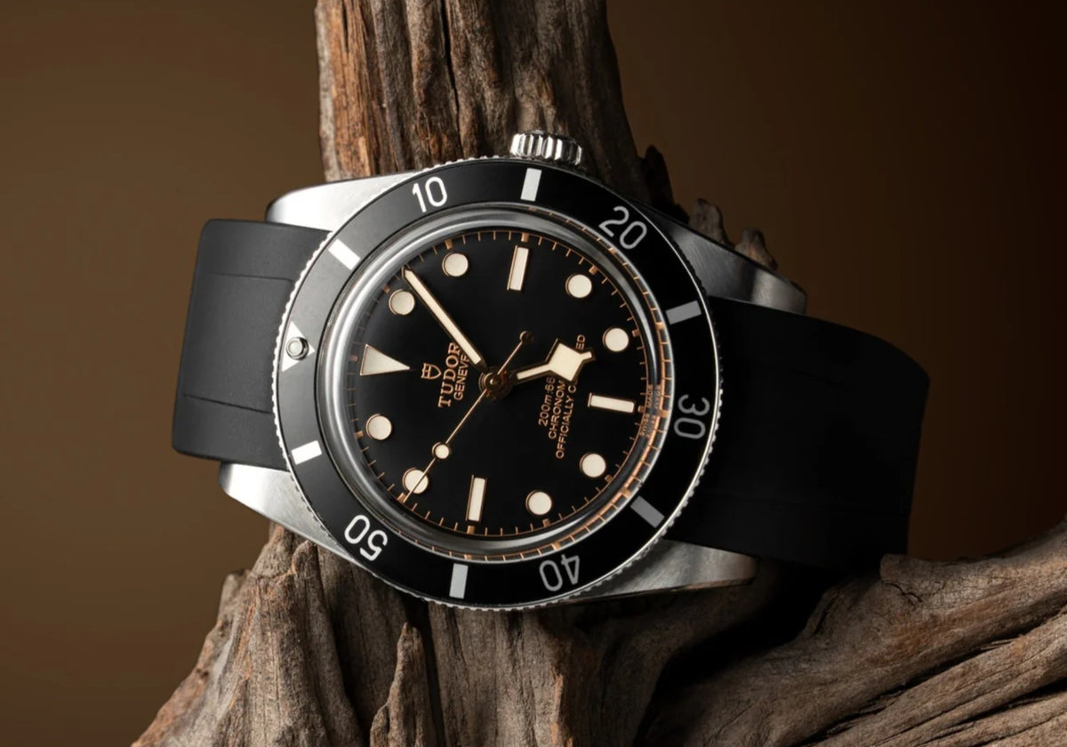 Tudor Black Bay on a black rubber strap resting against weathered wood, showing a luxury dive watch styled for everyday wear