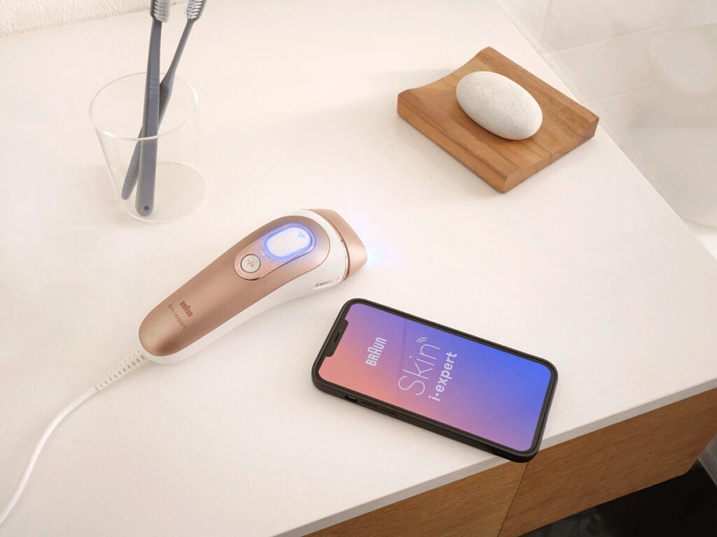 Braun Skin i-expert IPL device beside a smartphone on a bathroom counter.