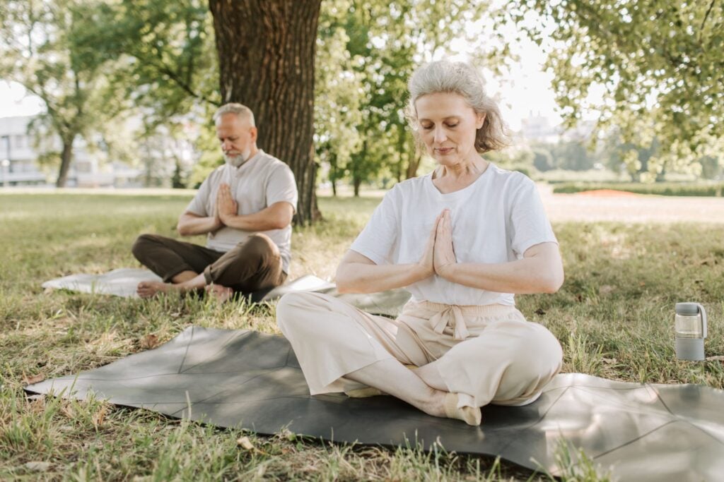 Elderly couple practicing yoga meditation outdoors, focusing on health and tranquility.